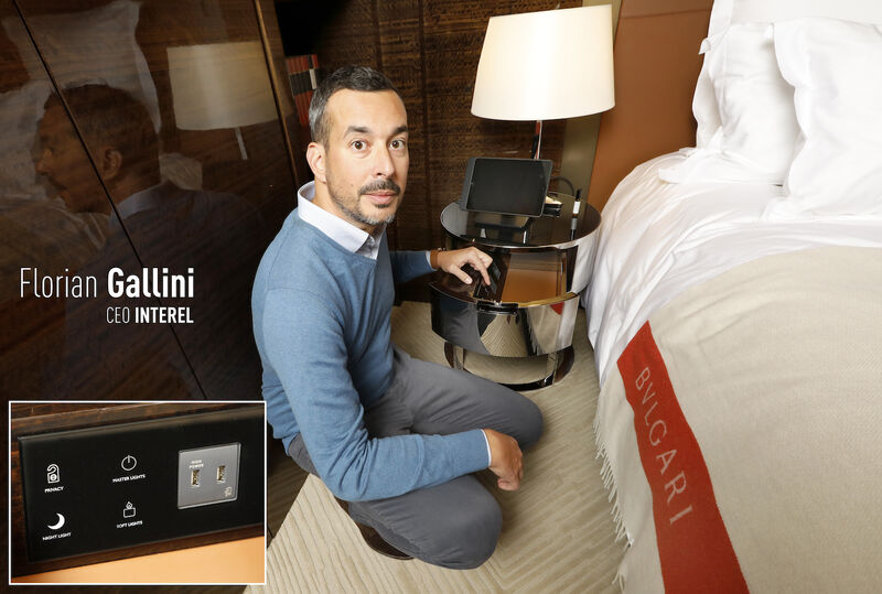 Florian Gallini kneeling beside a bed and demonstrating bedside controls at the Bulgari Hotel Paris
