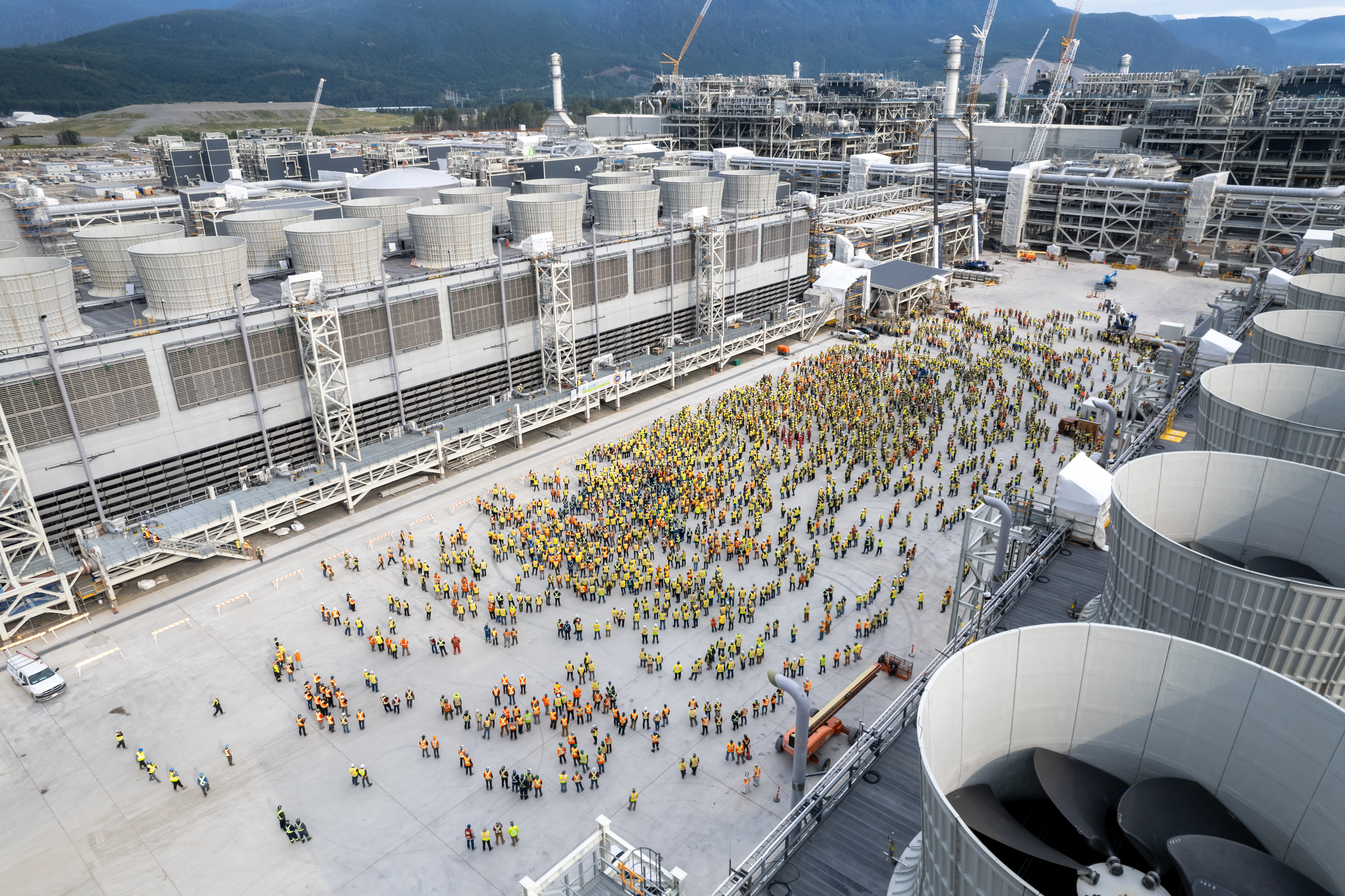 Construction workers gathered between cooling towers for a site-wide toolbox meeting at LNG Canada