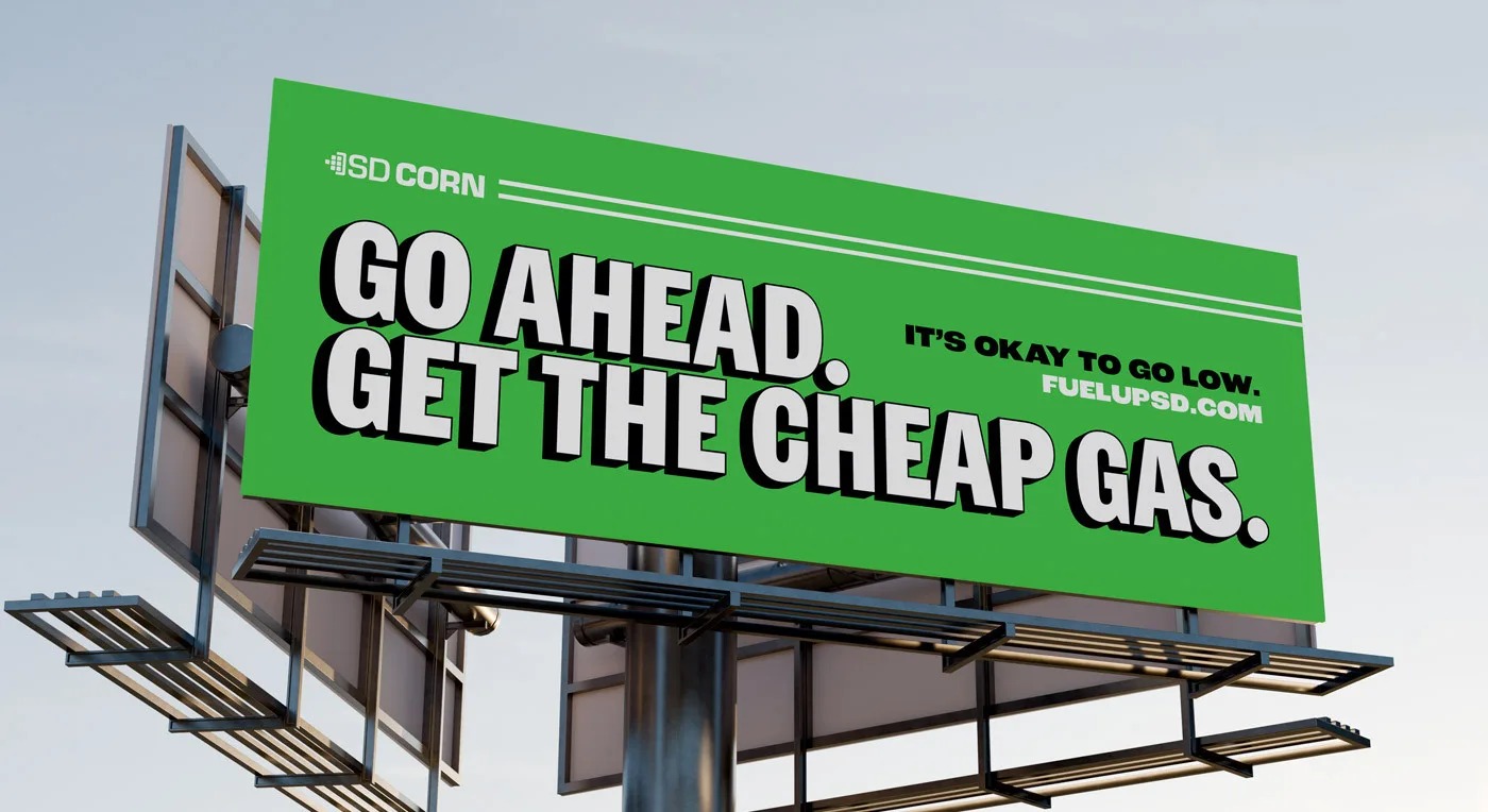 A South Dakota Corn campaign billboard promoting cheap gas beside an ethanol fuel pump