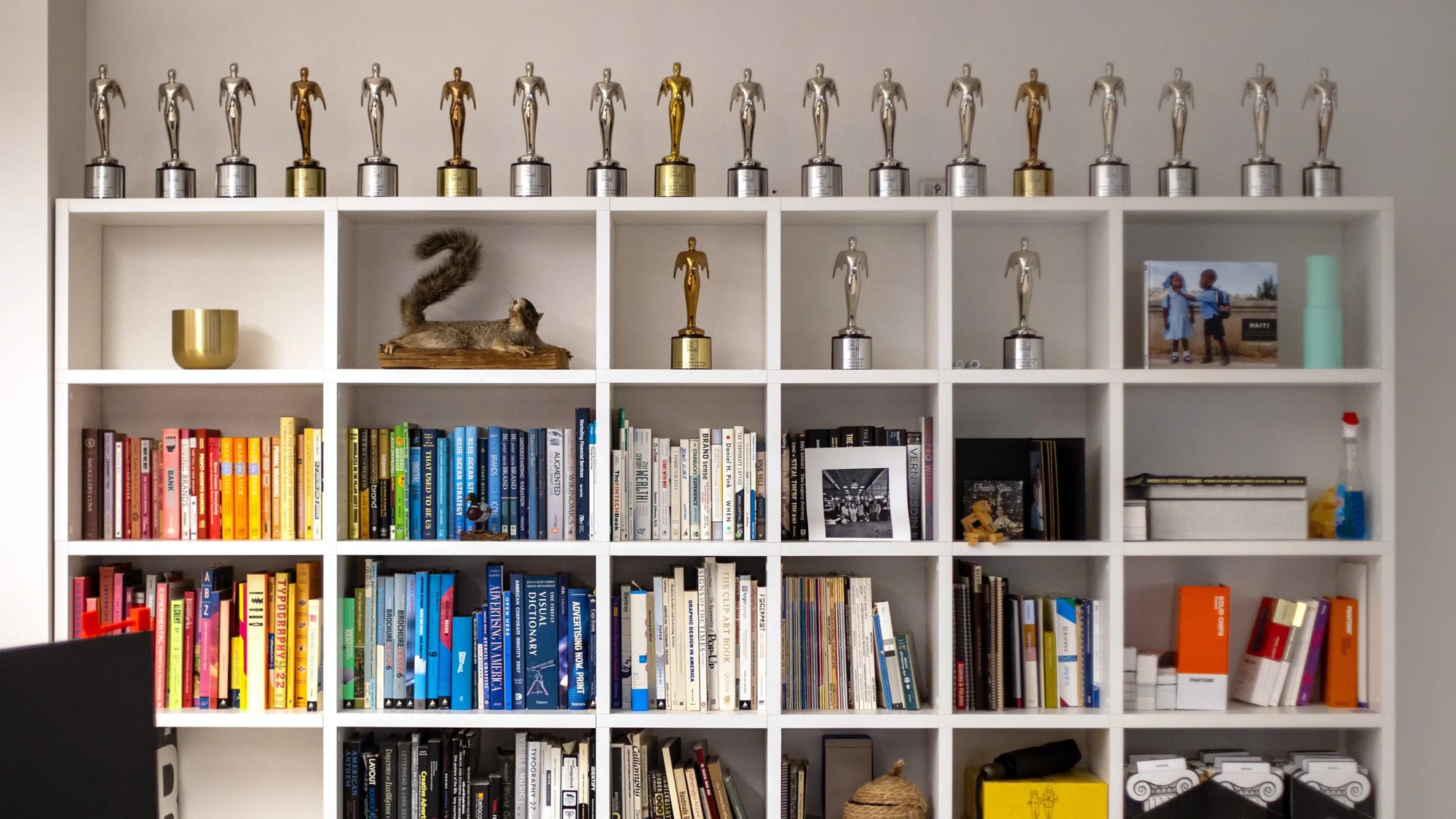 A wall of colorful design books and awards in the FMS office, with a squirrel on a shelf