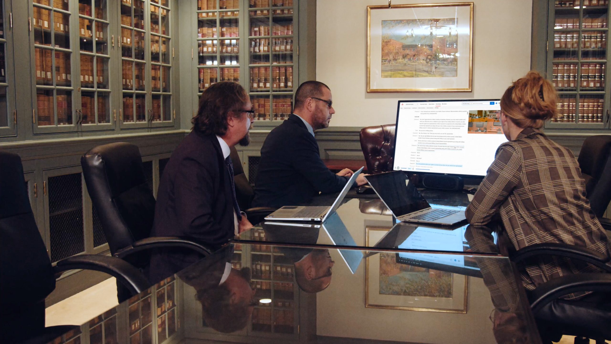 Three people reviewing a computer display in a library-like meeting room in a photograph published by For The Record
