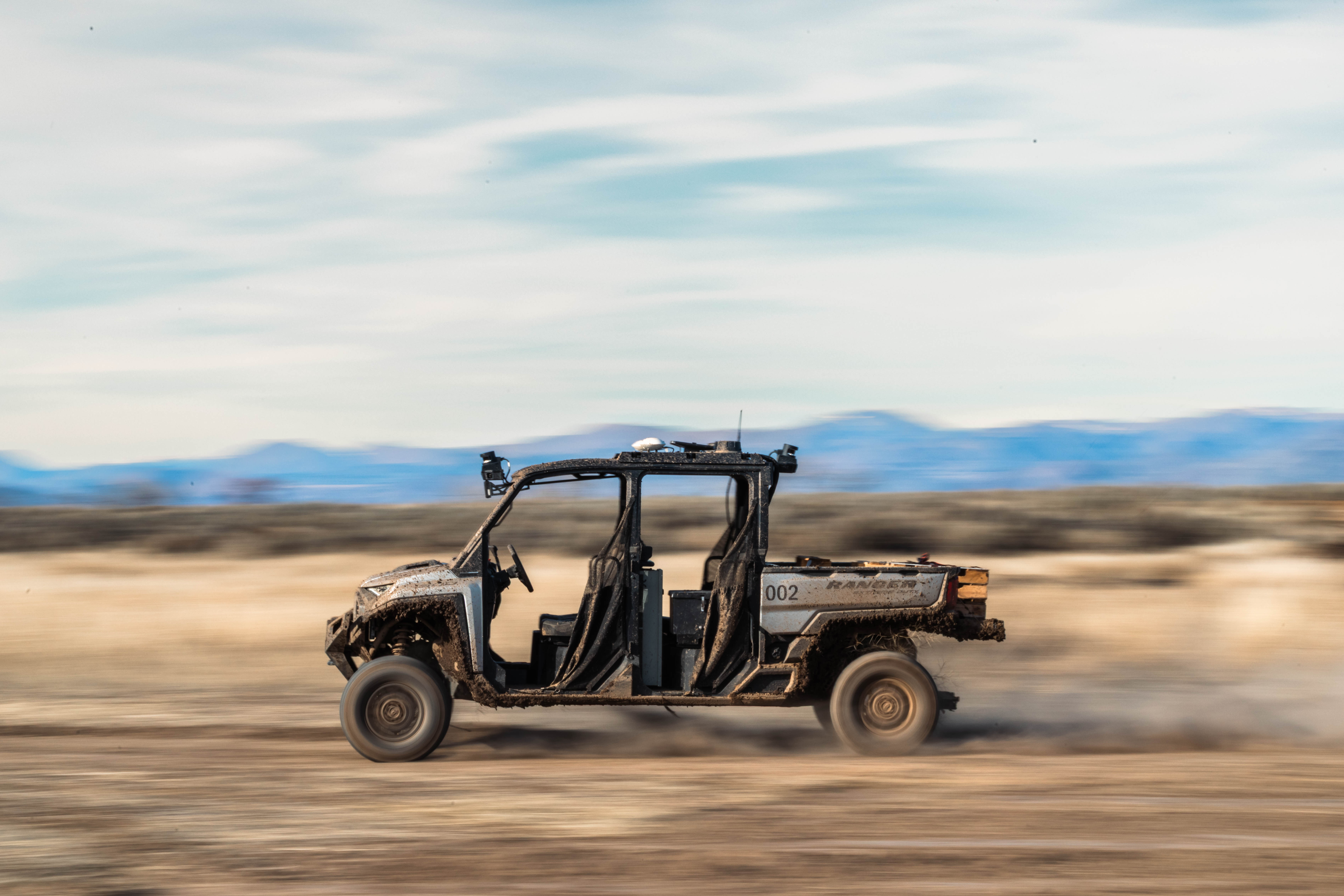 A mud-spattered Forterra Lancer moving across open ground with an empty driving seat