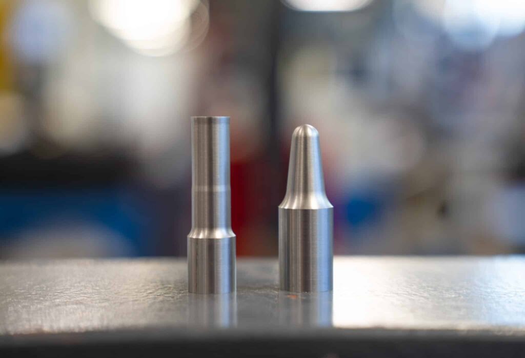 Two machined metal test parts standing on a workbench