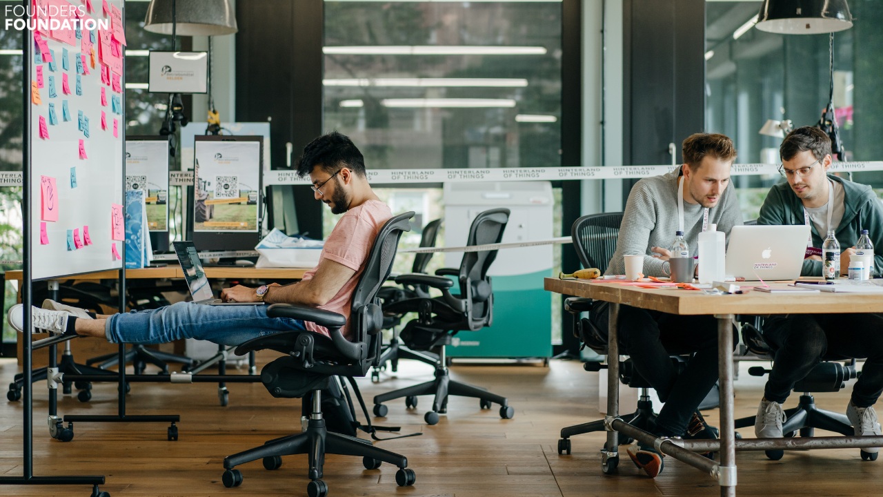 People working at desks beside a wall of colorful notes in Founders Home