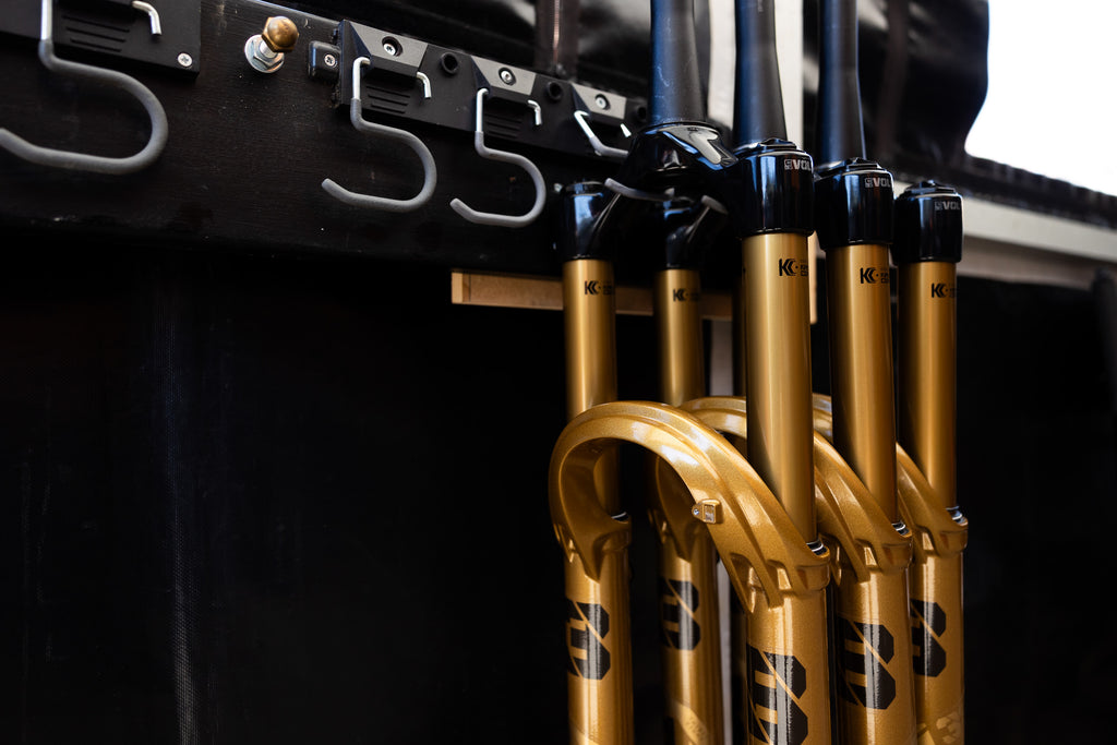 Gold FOX 38 suspension forks hanging from hooks in the World Cup enduro pits