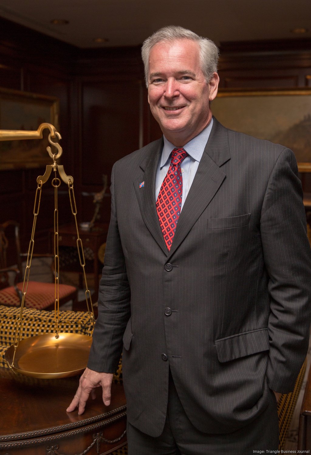 Frank Holding standing beside a brass balance scale in a wood-paneled office