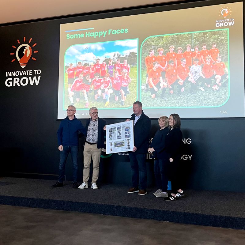 Frank Salmon with guests from Kiltimagh/Knock United at CMS's 2024 kickoff, in front of a screen showing youth football teams