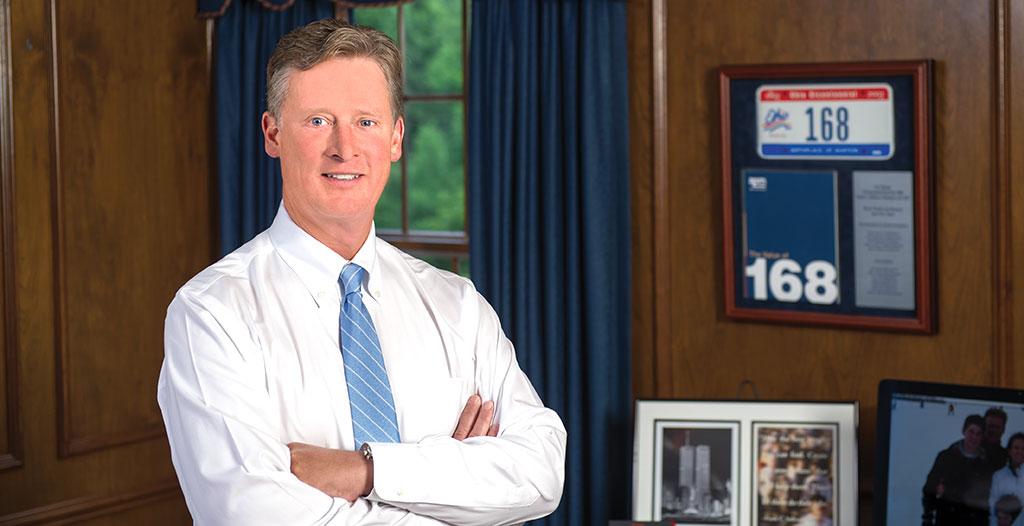 Archival photograph of Frank Sullivan in an office beside a framed license plate bearing the number 168