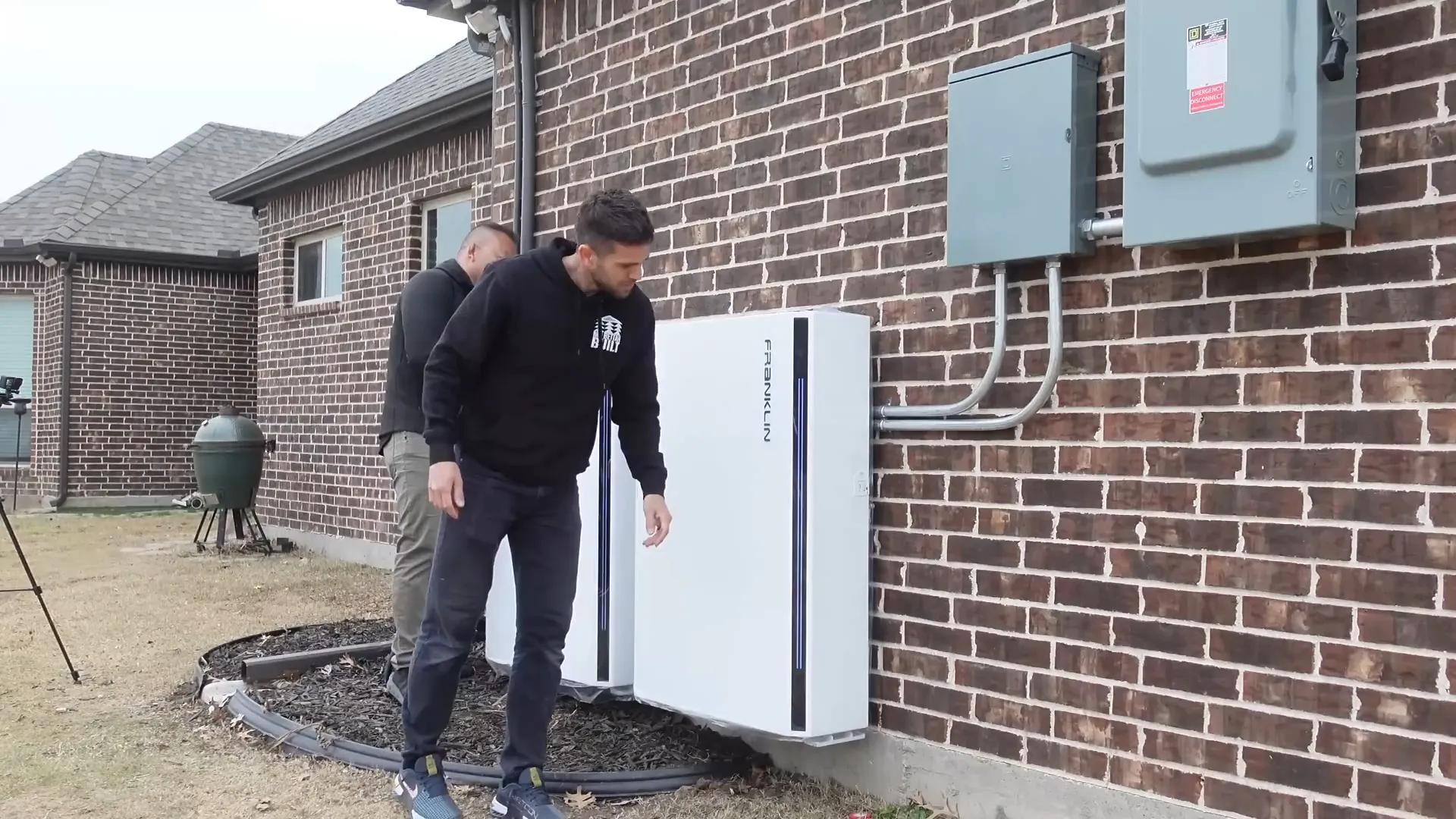 Two people beside two wall-mounted FranklinWH batteries at a brick house in Texas