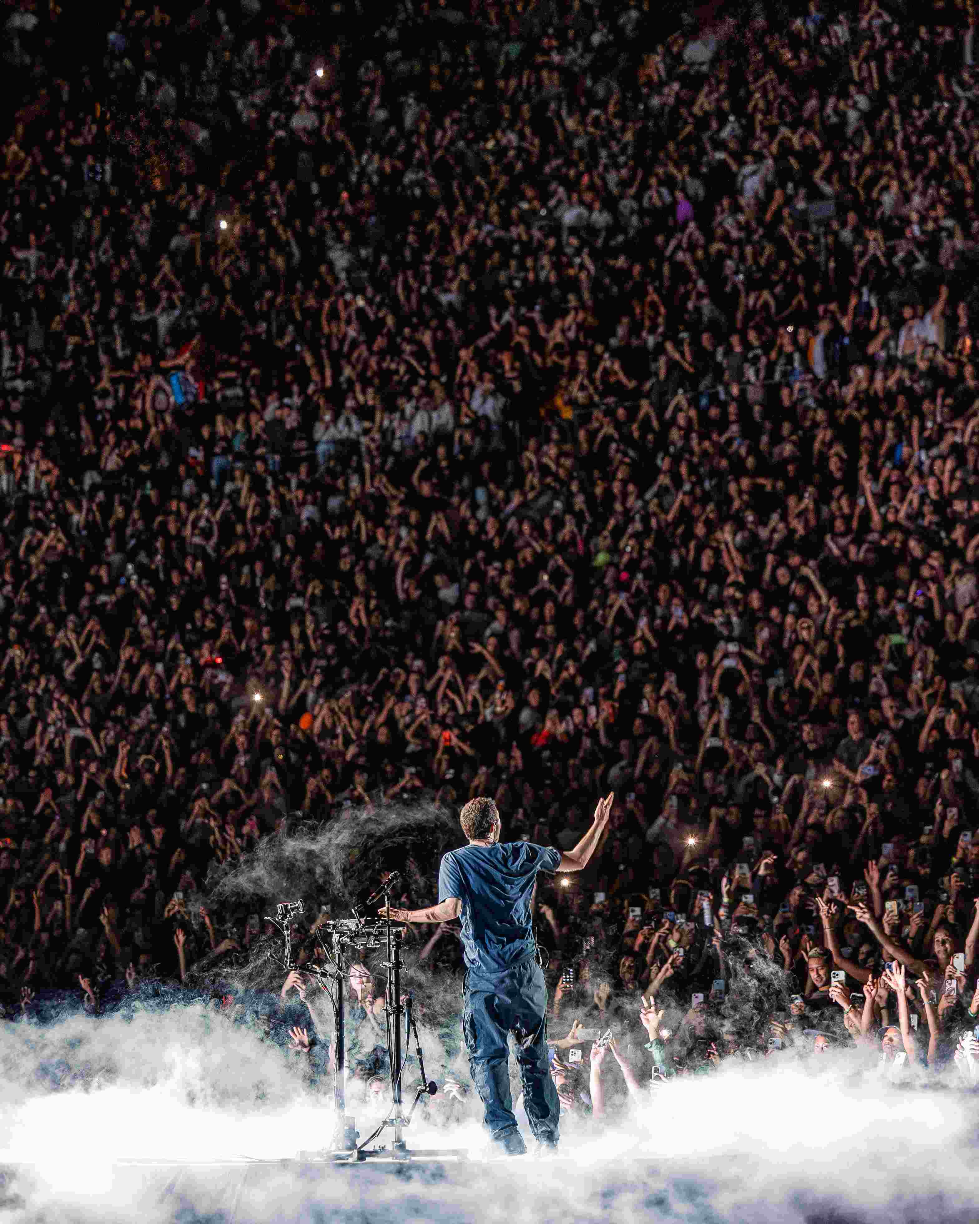 Fred again.. seen from behind onstage facing a vast illuminated audience