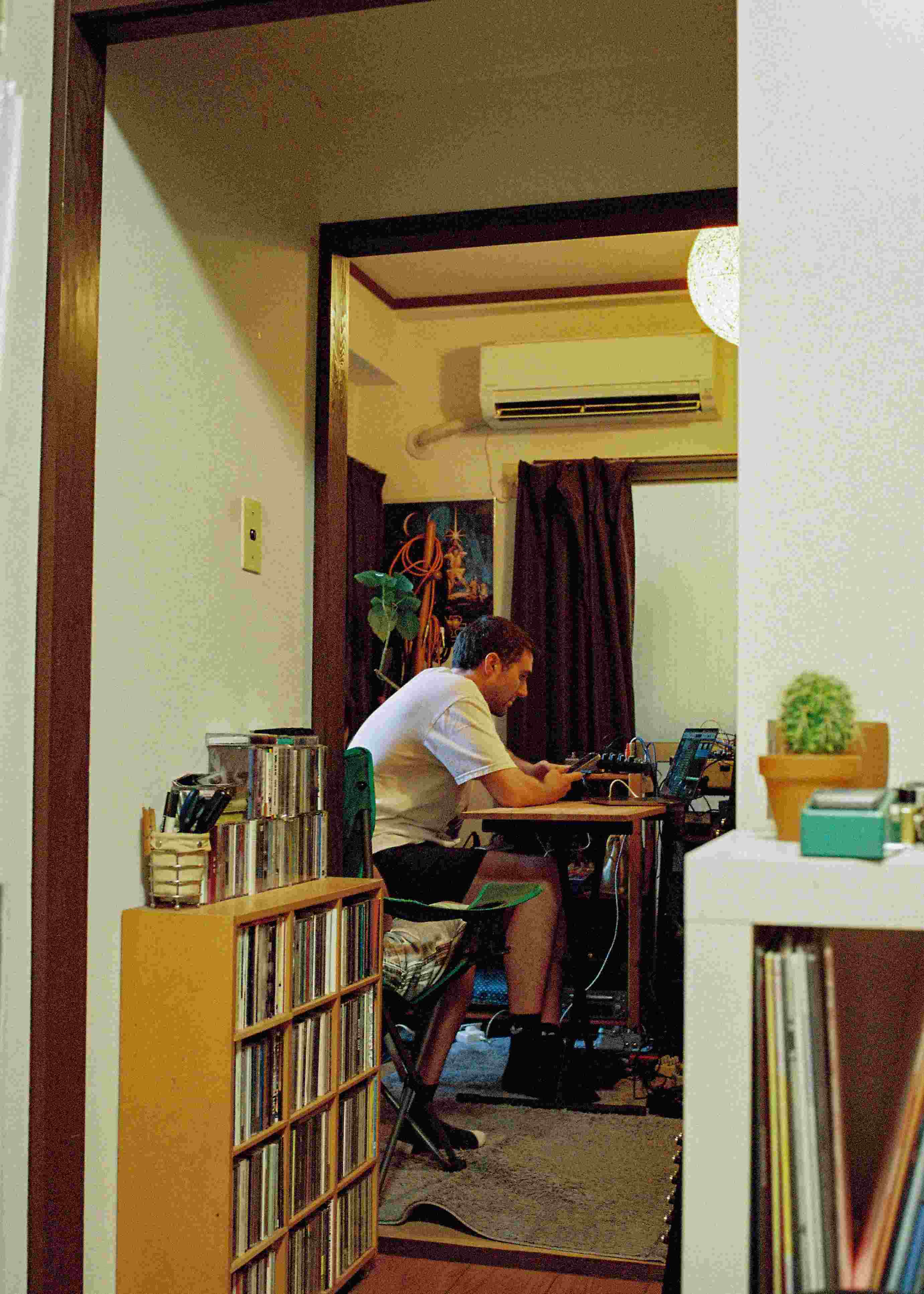 Fred again.. seated at a small table working with music equipment in a room lined with records