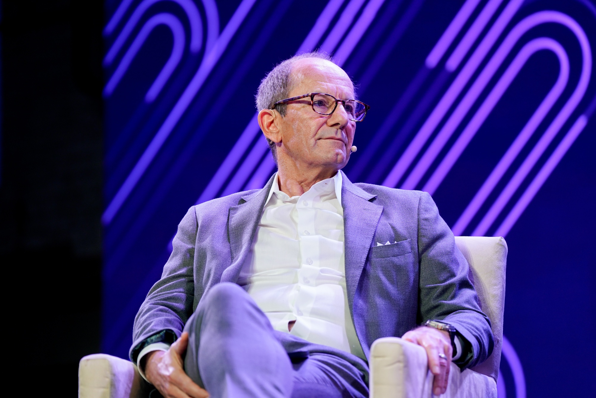 Fred Thiel seated onstage wearing a gray suit and a lapel microphone