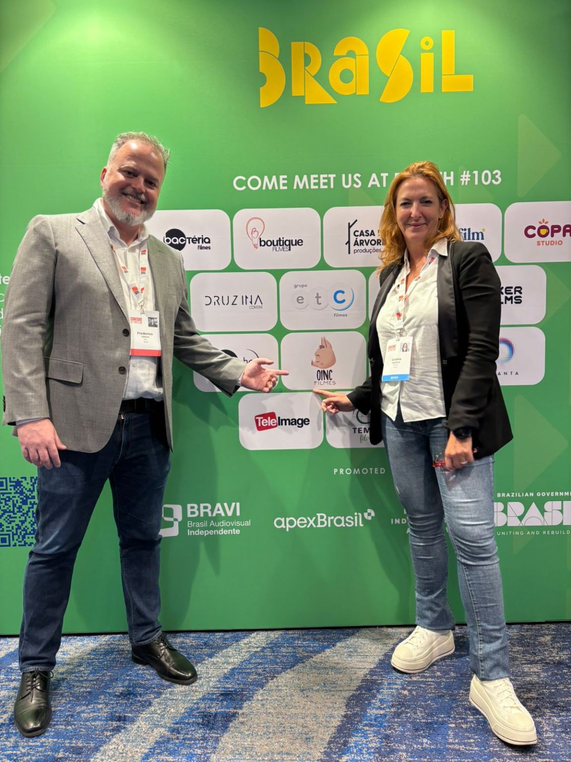 Fred Valente, left, and Juliana Algañaraz pointing to the Oinc Filmes logo at Content Americas in Miami.