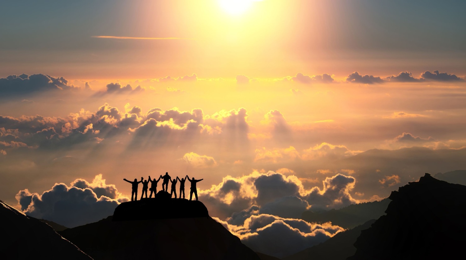 A group silhouetted on a mountain ridge beneath a bright sky