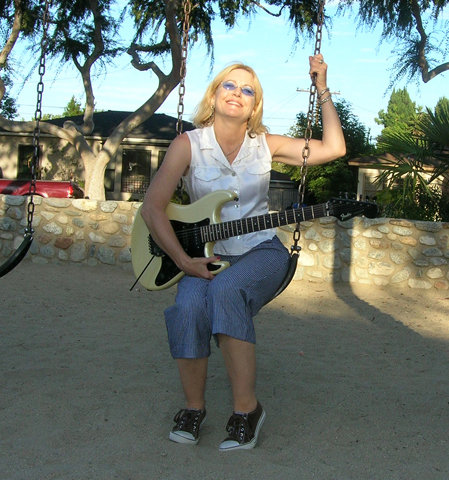Elizabeth Montague seated on a garden swing holding an electric guitar