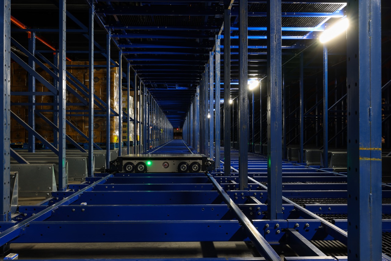 Automated pallet shuttle within tall blue warehouse racks at FreezPak