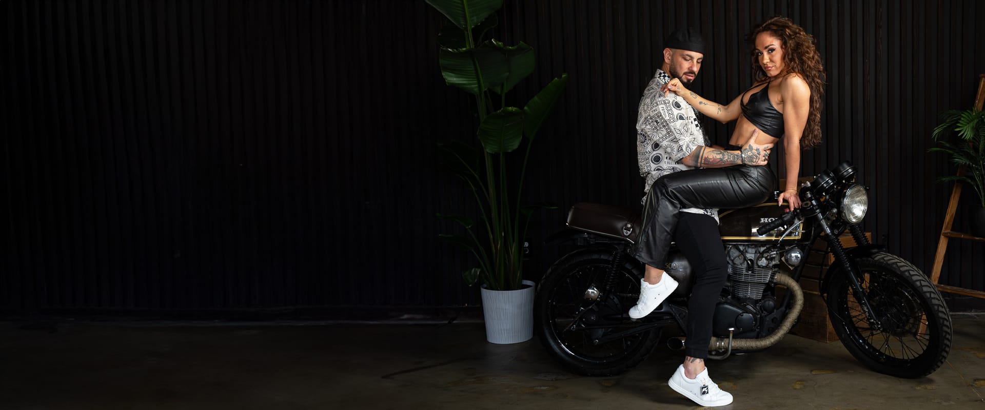 Two dancers wearing white Fuego sneakers pose beside a motorcycle