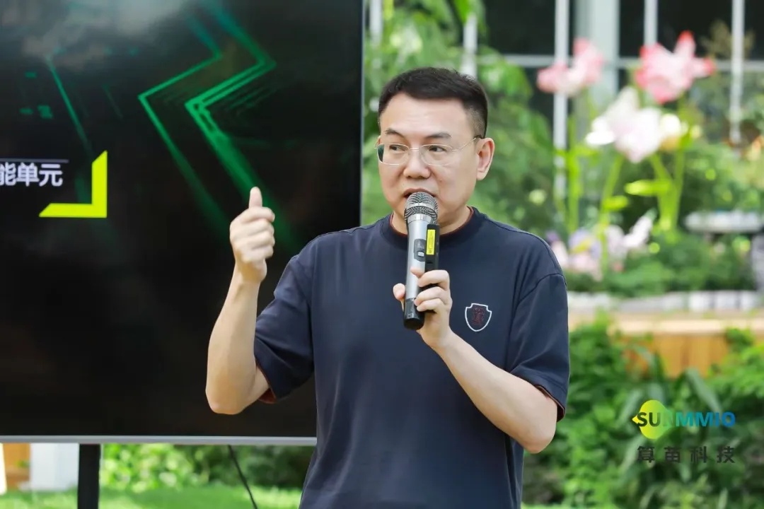Fuquan Wang, wearing glasses and a navy polo shirt, speaking into a microphone and gesturing with one hand.