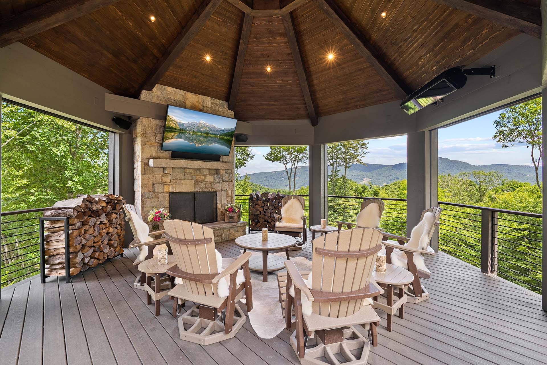 Covered mountain deck with a television mounted over a stone fireplace, Adirondack chairs, and Blue Ridge views