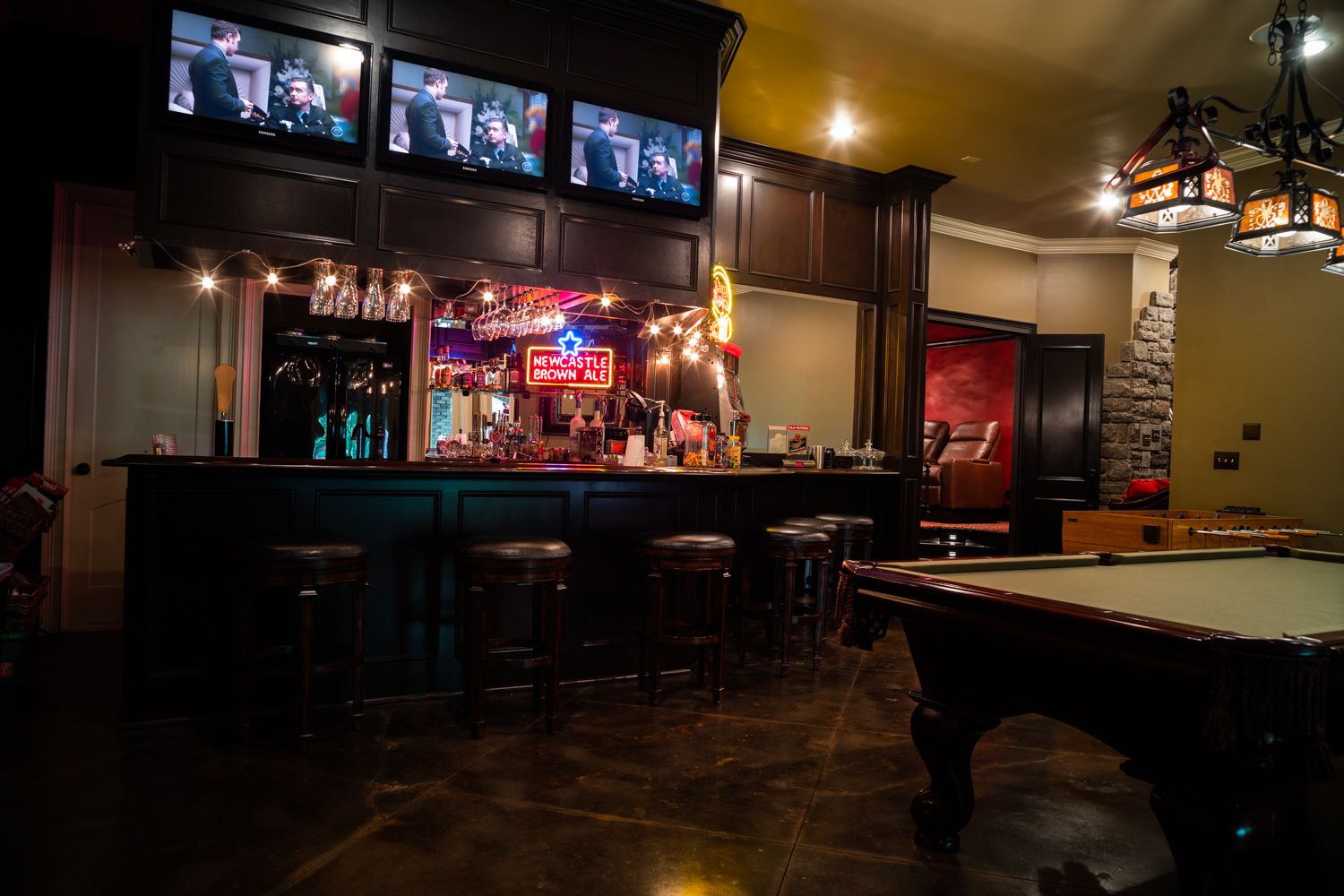 Basement pub and game room with a wall of televisions, wet bar, pool table and foosball table