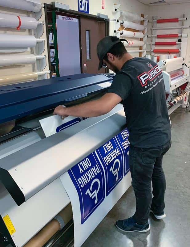 Fusion production worker operating a large-format printer producing blue parking signs