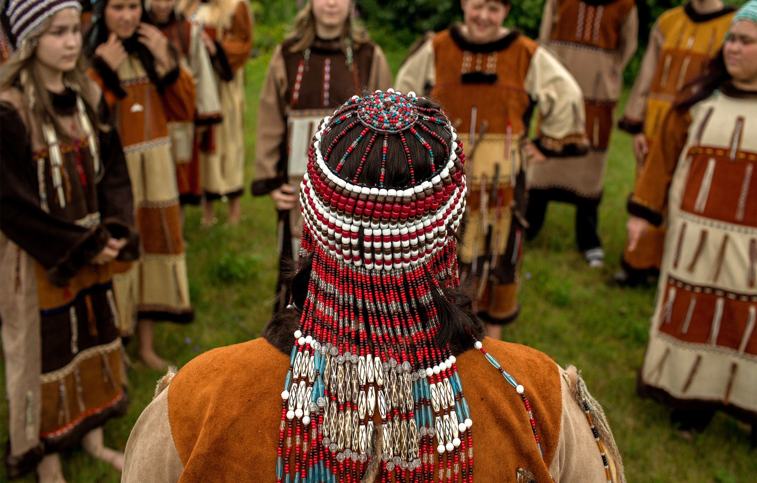 Alaska Native dancers gathered around a dancer wearing an intricate beaded headdress