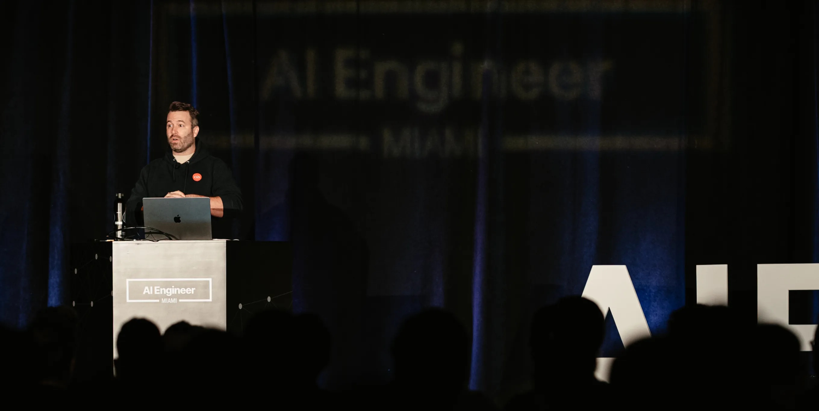 G2i founder Gabe Greenberg speaking behind a laptop at AI Engineer Miami
