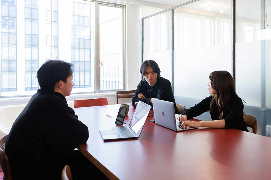 Three NEWB participants discussing work around a red table with laptops