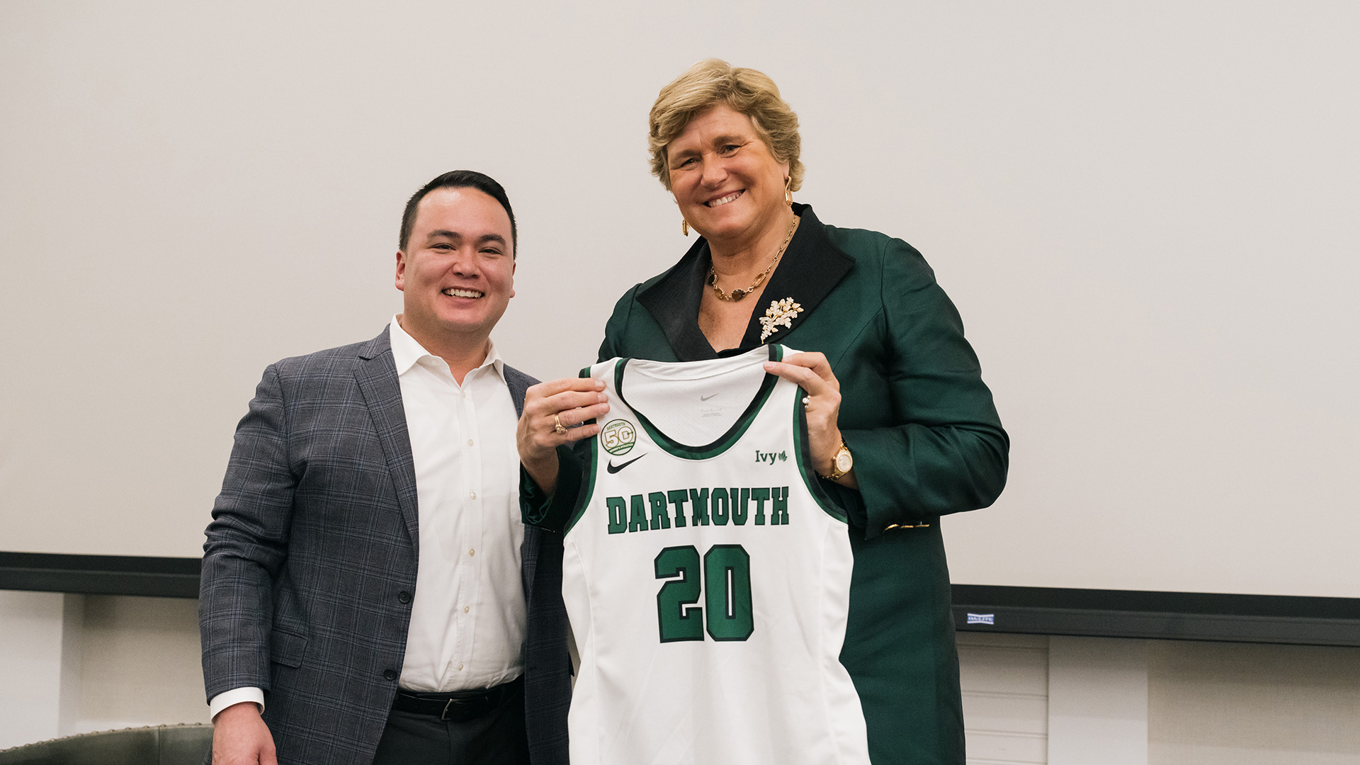Gail Boudreaux and Dartmouth athletics director Mike Harrity holding a Dartmouth number 20 basketball jersey