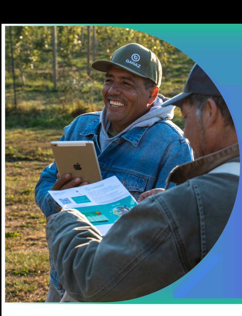 A farmworker in a Ganaz cap holds an iPad in the field while an employer reviews a Ganaz flyer.