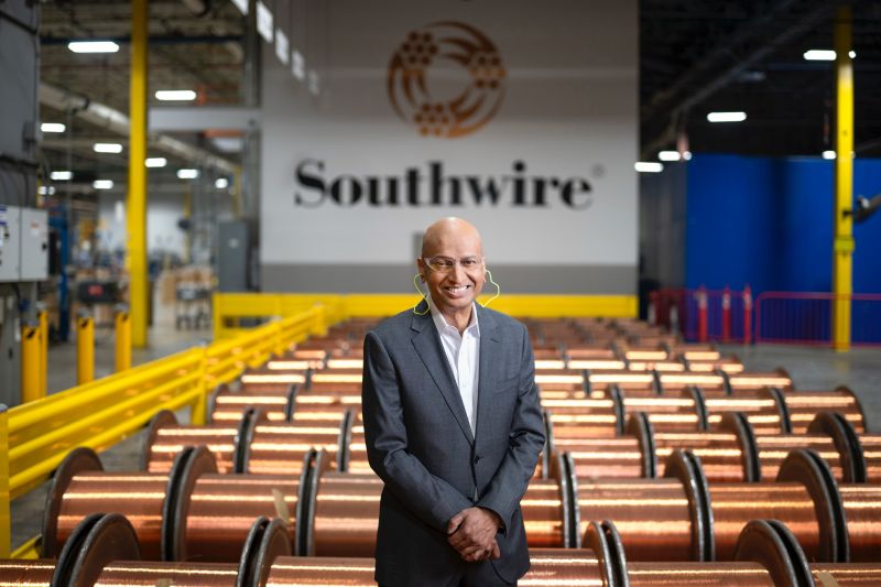 Ganesh Ramaswamy standing in a Southwire plant among large coils of copper wire