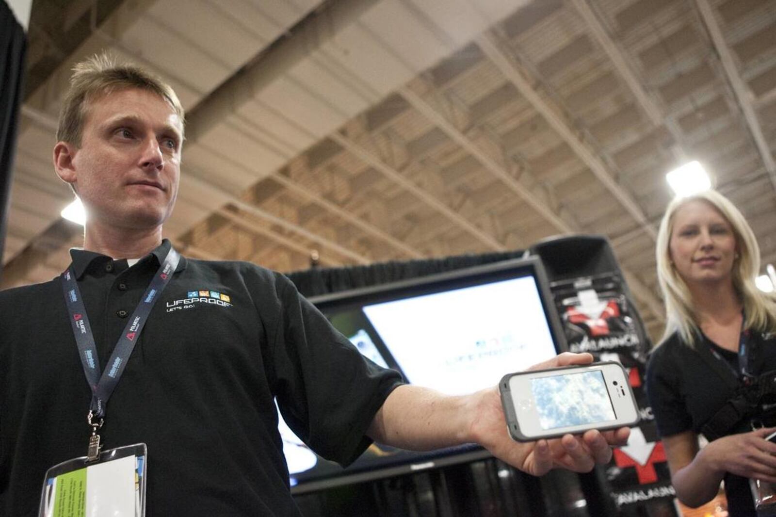 Gary Rayner holds a cased iPhone beside LifeProof event director Angel King at an outdoor trade show.