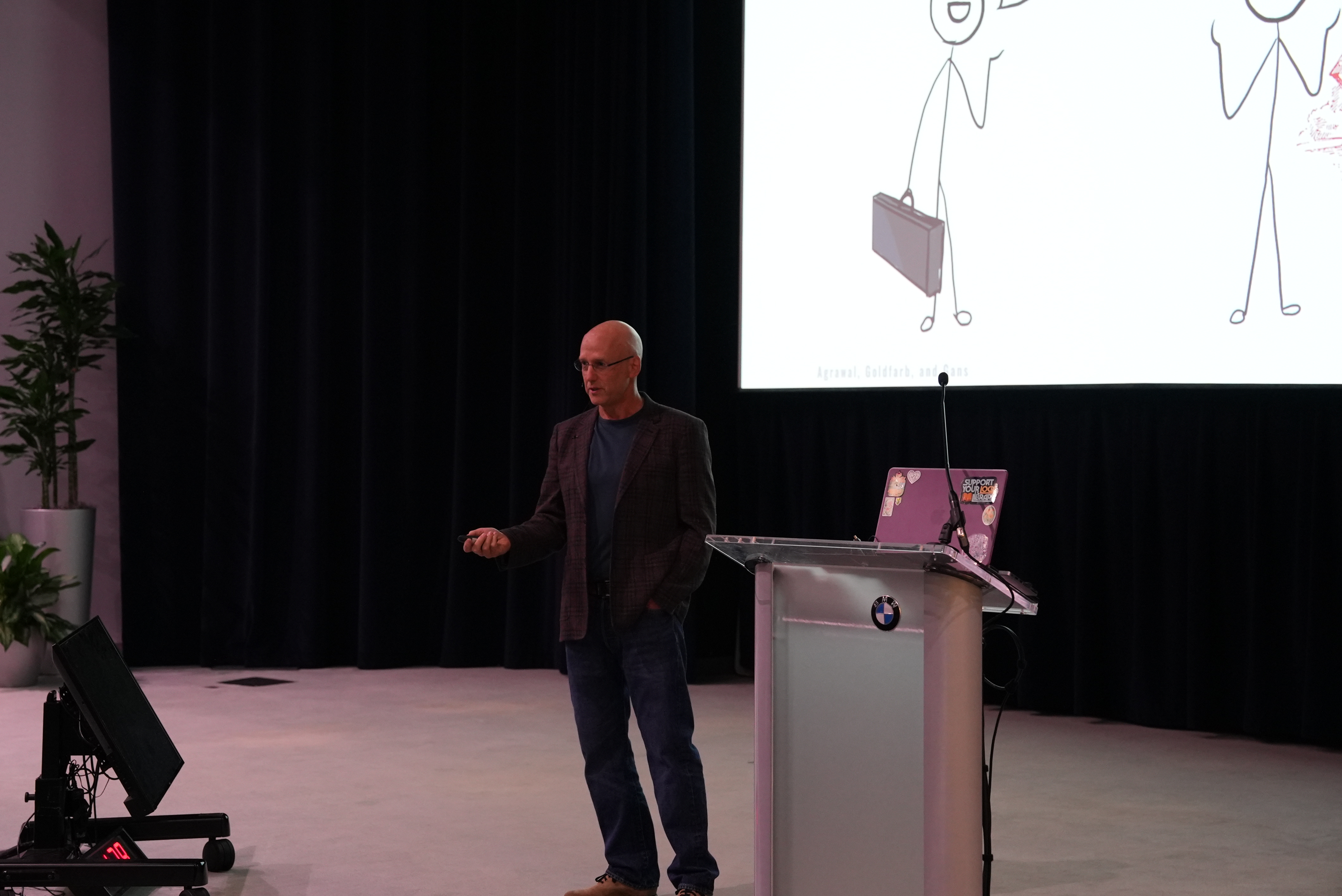 Gary Shiffman speaking beside a lectern and a projected illustration