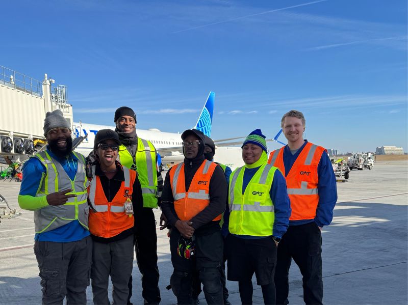 Six GAT team members in high-visibility vests on the ramp in Atlanta, with a United aircraft behind them.