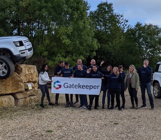 Gatekeeper colleagues at a UK team meetup, holding a company banner beside an off-road vehicle on stone blocks