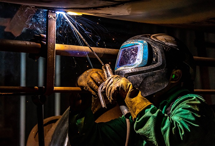 A worker wearing protective equipment welds beneath rail equipment