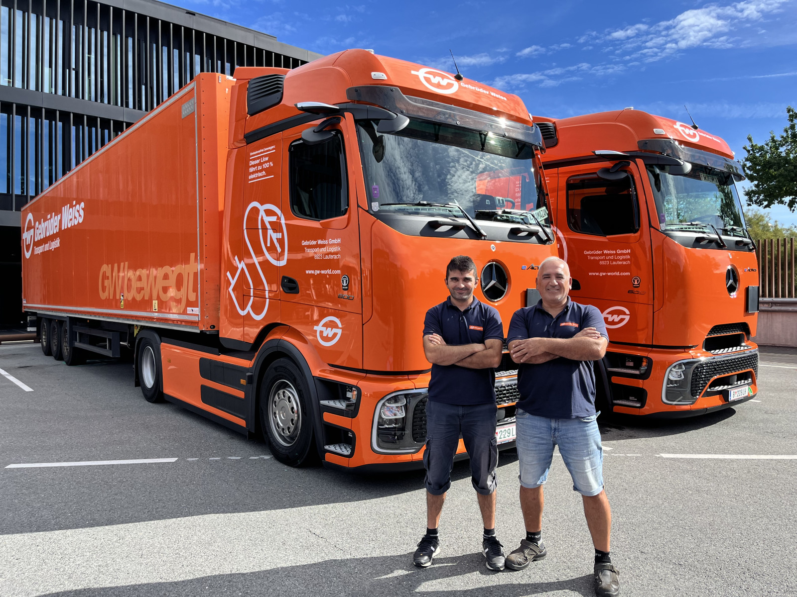 Two orange Gebrüder Weiss electric trucks outside the company's Lauterach offices