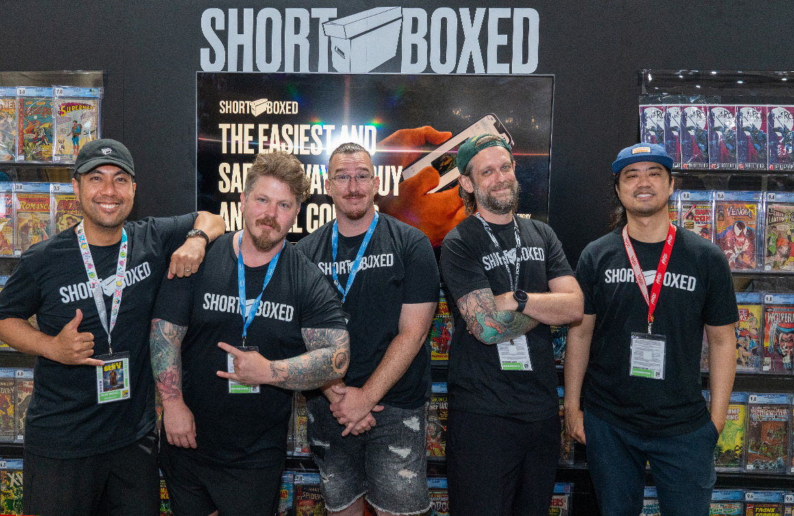 The Shortboxed team standing at a comic convention booth filled with comics