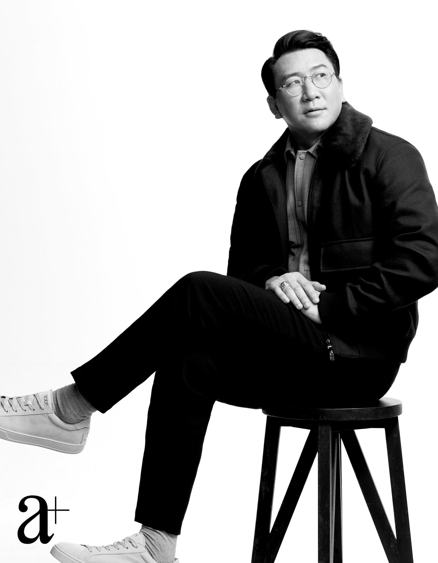 Gene Yu seated during an a+ Singapore editorial photo shoot, wearing glasses and a jacket