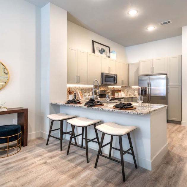 A Modera Midtown Dallas kitchen with Shaker cabinet doors, a granite island, and three stools