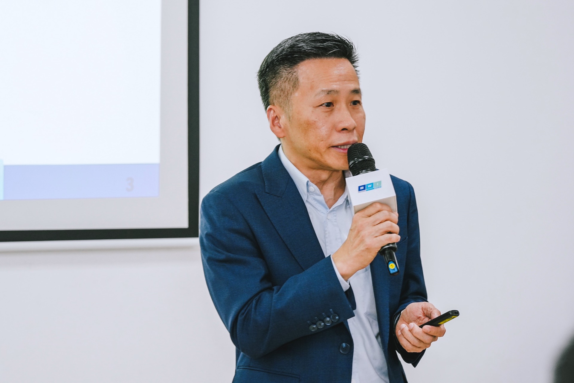 George Chang speaking into a microphone and holding a presentation remote at BWI