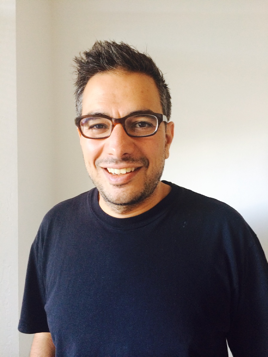 An archival photograph of George Favvas wearing glasses and a dark T-shirt