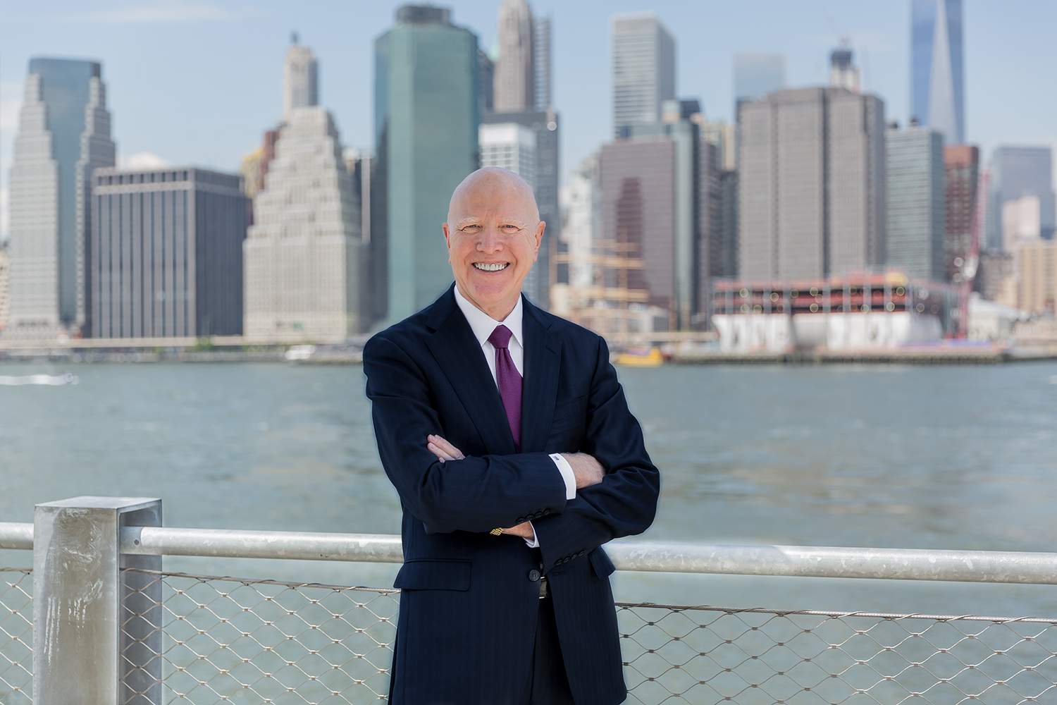 George Gleason standing by the waterfront with a city skyline behind him