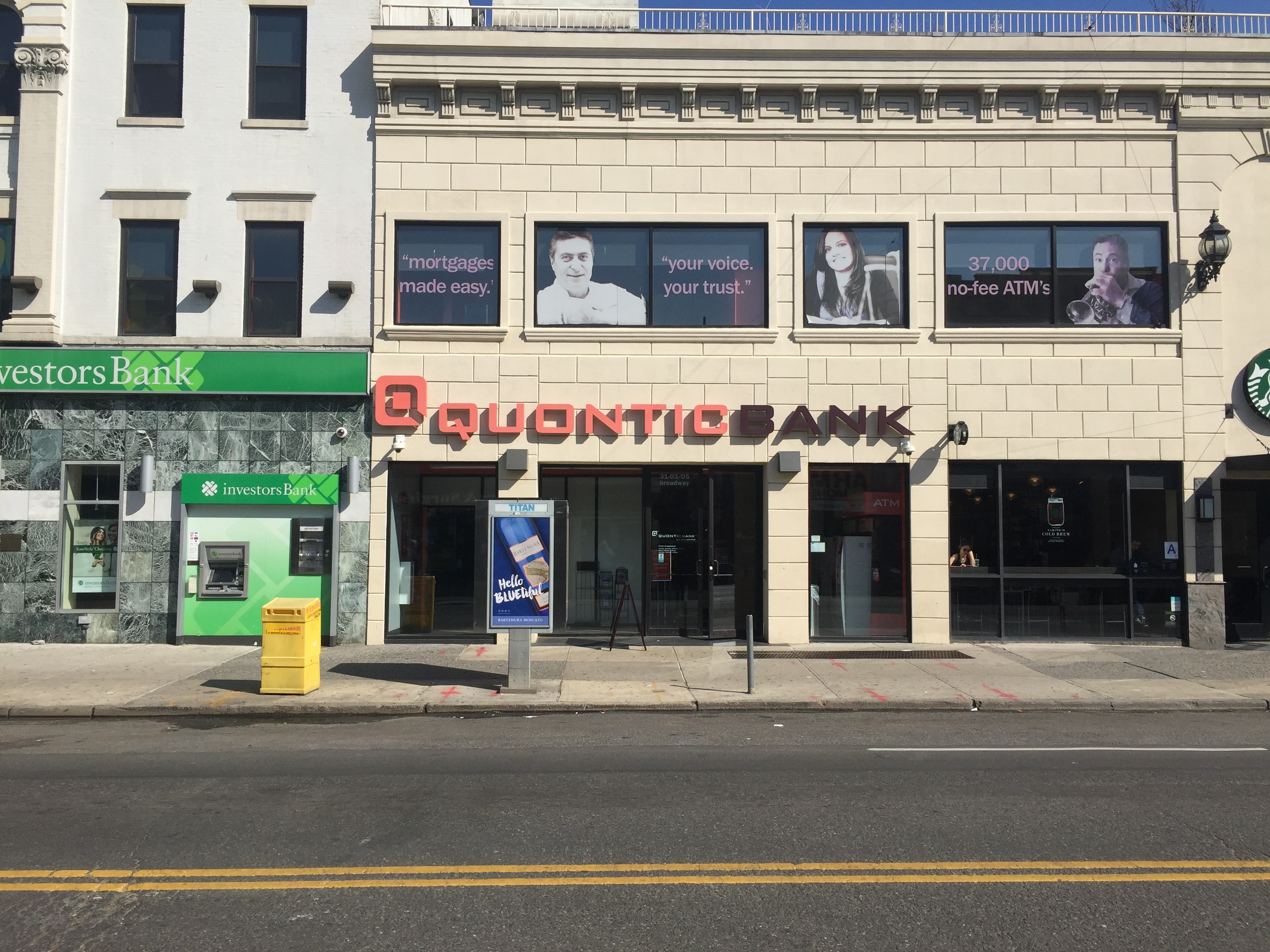 Quontic Bank’s Astoria storefront with orange lettering, photographed from across Broadway
