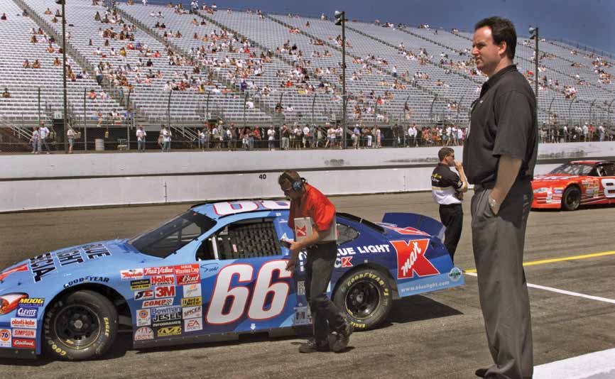 George Pyne standing beside a stock car at a NASCAR track