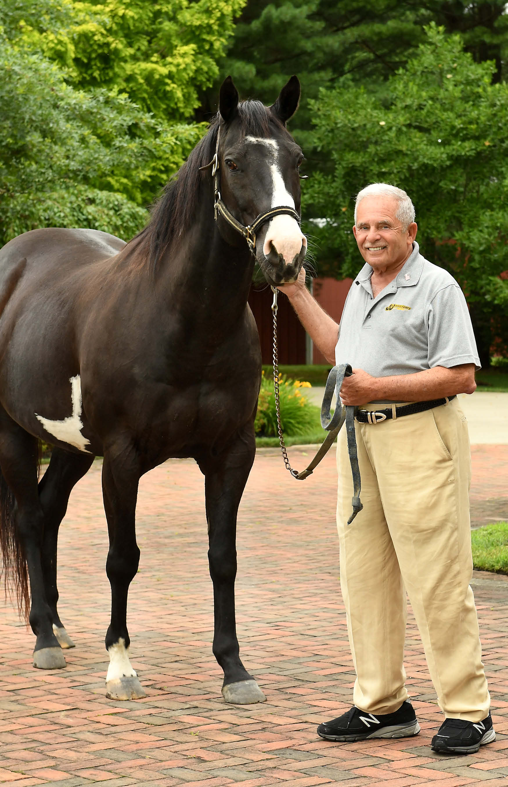 Gerry Shreiber standing beside his horse Black Jack on a brick path