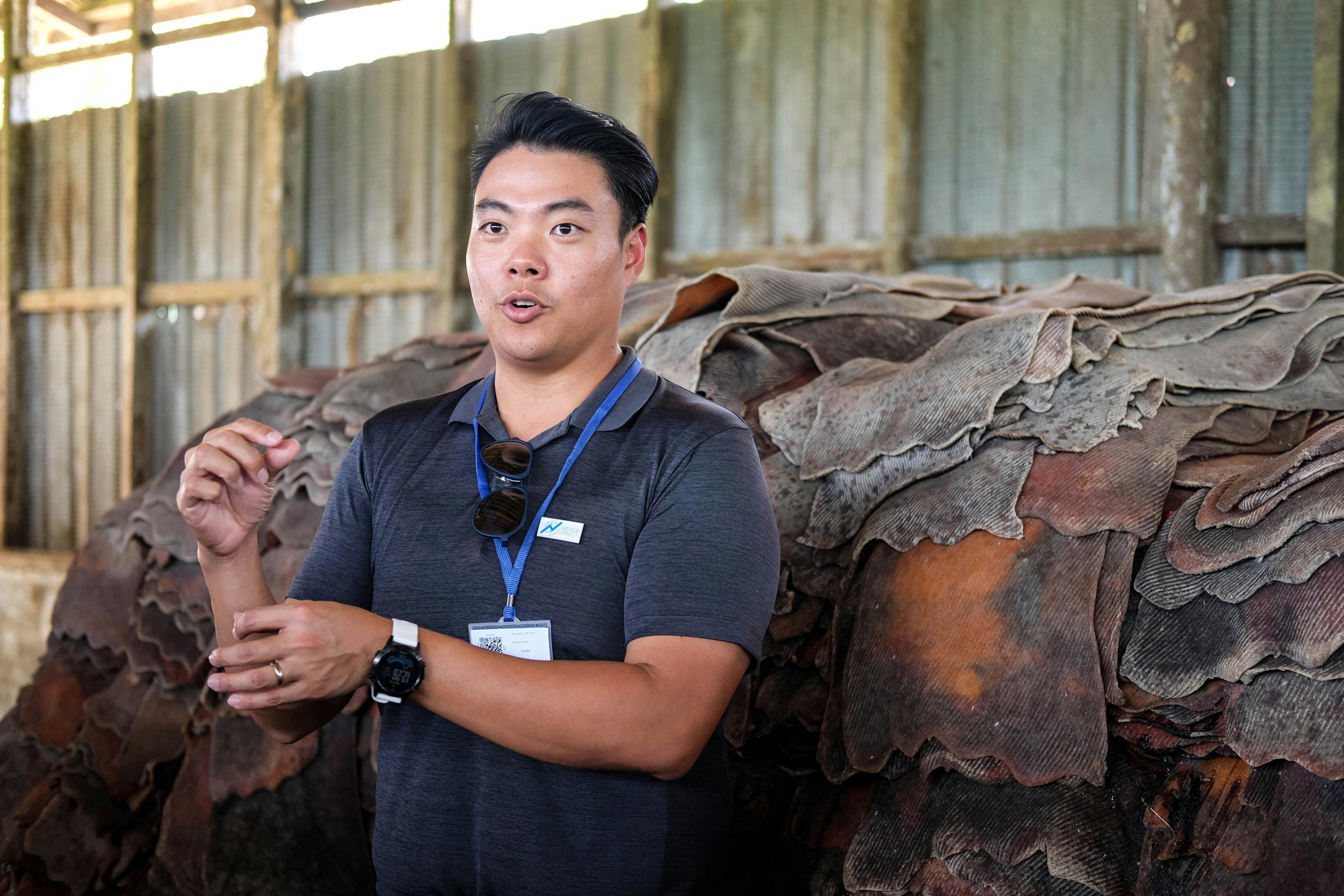 Gerald Tan speaking beside stacks of rubber in a factory