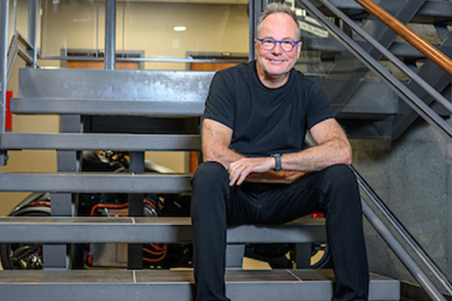 Ghyslain Goulet in a T-shirt and jeans, seated on stairs inside ACET headquarters.