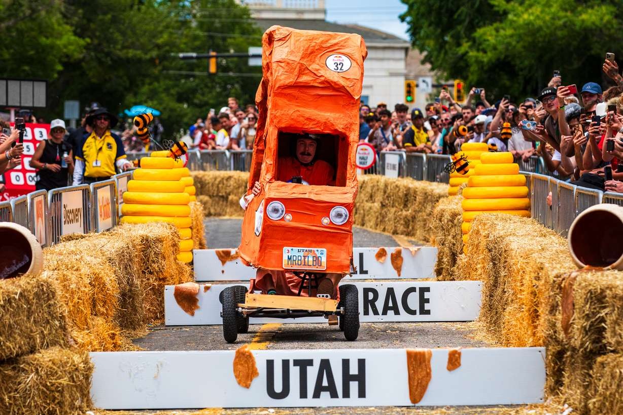 The orange Delicate Arch soapbox cart clears an obstacle between hay bales as a crowd watches in Salt Lake City.