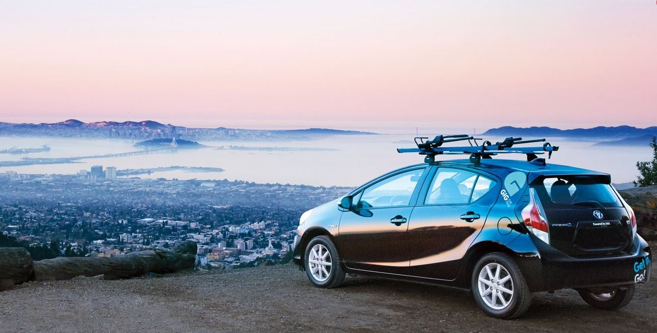 A black GIG Prius C with blue roof-mounted bicycle racks overlooking San Francisco Bay